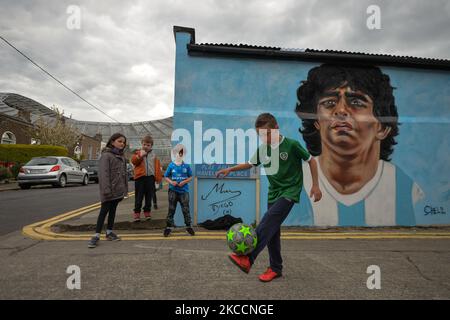 Johnny Figo Murphy, 9 Jahre alt, zeigt seine Fußballschuhe vor einem neuen Wandgemälde von CHELS (Chelsea Jacobs, ein in Dublin lebender amerikanischer Künstler), der Diego Maradona, einen der größten Spieler in der Geschichte des Fußballs, vertritt. Am Dienstag, den 13. April 2021, in Dublin, Irland. (Foto von Artur Widak/NurPhoto) Stockfoto