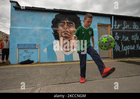 Johnny Figo Murphy, 9 Jahre alt, zeigt seine Fußballschuhe vor einem neuen Wandgemälde von CHELS (Chelsea Jacobs, ein in Dublin lebender amerikanischer Künstler), der Diego Maradona, einen der größten Spieler in der Geschichte des Fußballs, vertritt. Am Dienstag, den 13. April 2021, in Dublin, Irland. (Foto von Artur Widak/NurPhoto) Stockfoto