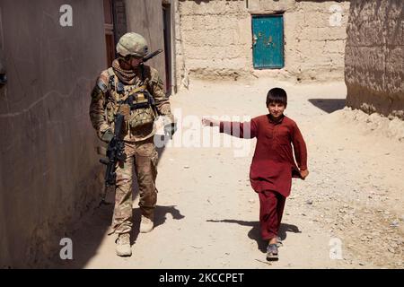 US-Armeesoldat geht auf einer Patrouille in Afghanistan an der Seite eines Jungen. Stockfoto