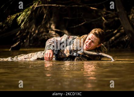 Ein simulierter verwundeter Soldat ruft um Hilfe, die im Fluss liegt. Stockfoto