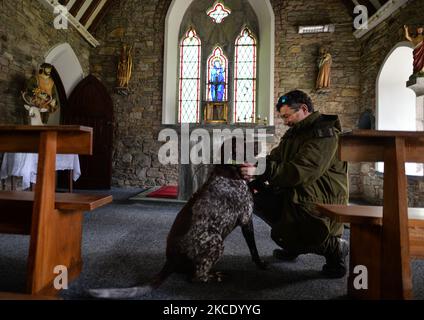 Pater Krzysztof Sikora mit seinem Hund 'Rambo' in der Ballynahinch Kirche in Emlaghdauroe, Connemara. Diese ehemalige Kirche der irischen Kirche aus dem Jahr 1865, heute bekannt als St. Hubert, der schutzpatron der Jäger, liegt in der spektakulärsten Landschaft der Berge, Moor und Seen. Die Gemeinde Roundstone gilt geografisch als die größte Gemeinde Irlands und erstreckt sich von den Stränden von Gurteen bis zu den zwölf Bens und dem Mám Tuirc-Gebirge. Bis zum 1990s wurde die Pfarrei von drei Priestern gedient, jetzt gibt es nur noch einen, der fünf Kirchen betreut. Der derzeitige Pfarrer, ein polnischer Pfarrer Krzyszt Stockfoto