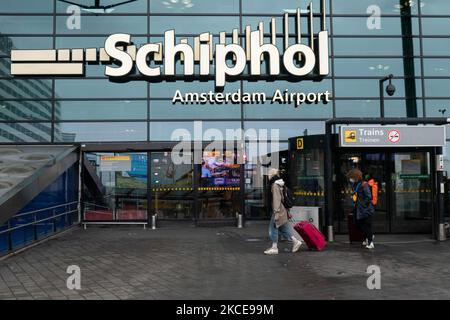 Eingang zum Flughafen Schiphol mit Menschen, die Gesichtsmaske tragen. Internationaler Flughafen Amsterdam Schiphol während der Pandemie Covid-19. Die Anzahl der Passagiere und die Crew tragen Schutzausrüstung wie die obligatorischen Gesichtsmasken und Handschuhe, um die Ausbreitung des Coronavirus zu vermeiden. Die Zahl der Passagiere im Weltflug sank aufgrund der Reisebeschränkungen, Sicherheitsmaßnahmen wie Sperren, Quarantäne, PCR und Schnelltests vor den Flügen während der Ära der Coronavirus-Pandemie Covid-19, die die Luft- und Reisebranche schwer getroffen hatte. Amster Stockfoto