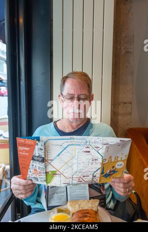 Senior mit Stadtplan und Stadtführer von Paris, sitzt im Café. Stockfoto