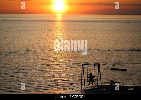 Ein Mädchen sitzt während des Sonnenuntergangs auf einer Schaukel am Ufer des Finnischen Meerbusens. Die Lufttemperatur in St. Petersburg stieg auf 25 Grad. Sankt Petersburg, Russland 13. Mai 2021 (Foto von Valya Egorshin/NurPhoto) Stockfoto