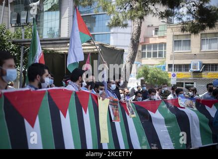 Iranische Männer mit Schutzmasken stehen während einer Protestveranstaltung auf dem Palästinenserplatz im Zentrum von Teheran am 18. Mai 2021 hinter palästinensischen Fahnen, um den israelischen Raketenangriff auf Gaza und die Tötung von Kindern zu verurteilen. (Foto von Morteza Nikoubazl/NurPhoto) Stockfoto