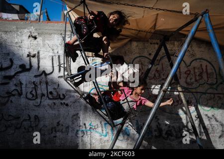 Ein Palästinenser wacht am 24. Mai 2021 nach einem Waffenstillstand zwischen Israel und der Hamas über Kinder, die in einem beschädigten Viertel in Beit Hanoun im nördlichen Gazastreifen auf einer Schaukel spielen. - Ende der vergangenen Woche wurde Nach 11 Tagen tödlicher Gewalt zwischen Israel und der Hamas-Bewegung, die Gaza führt, Ein Waffenstillstand erreicht. Durch den Waffenstillstand wurde die verheerende Bombardierung Israels auf die überfüllte palästinensische Küstenenklave gestoppt, bei der nach Angaben des Gesundheitsministeriums von Gaza 248 Palästinenser, darunter 66 Kinder, getötet und mehr als 1.900 Menschen verletzt wurden. Unterdessen forderten Raketen aus Gaza 12 Menschenleben in ISR Stockfoto