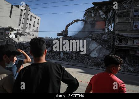 Am 08. Juni 2021 schauen Palästinenser mit Schutzmasken auf ägyptische Arbeiter und Maschinen, die die Trümmer der zerstörten Türme und Häuser in Gaza-Stadt entfernen. Ägypten gab am 04. Juni bekannt, dass es Arbeiter und Ausrüstung entsendet, um nach den Kämpfen zwischen Israel und Aktivisten im Gazastreifen beim Wiederaufbau zu helfen. (Foto von Majdi Fathi/NurPhoto) Stockfoto