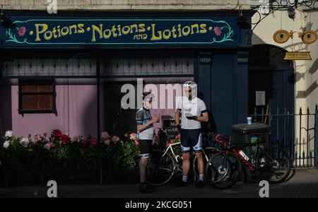 Zwei Radfahrer genießen einen Drink vor einer mit Blumen geschmückten lokalen Apotheke im Dorf Enniskerry, Co. Wicklow. Es sind nur noch zwei Tage, bis die Dreharbeiten für Disneys „enttäuschte“ Hauptrolle mit Amy Adams, Patrick Dempsey, James Marsden, Idina Menzel und Maya Rudolph beginnen. Ein Team von Zimmerleuten, Malern, Baumeistern und Dekorateuren hat den letzten Schliff gegeben, um Teile des Dorfes wie ein magisches Disney-Wunderland aussehen zu lassen. Am Freitag, den 11. Juni 2021, in Enniskerry, County Wicklow, Irland. (Foto von Artur Widak/NurPhoto) Stockfoto