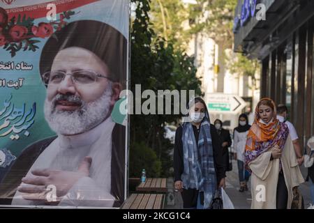 Zwei iranische Frauen gehen an dem Wahlbanner eines Präsidentschaftskandidaten Ebrahim Raisi vorbei, das während der Tage der Präsidentschaftswahlen im Iran am 12. Juni 2021 an einer Straßenseite aus einem Raisi-Wahlkampfzentrum im Norden Teherans gehängt wird. (Foto von Morteza Nikoubazl/NurPhoto) Stockfoto