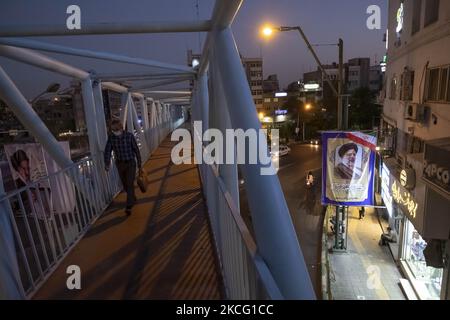 Ein iranischer Mann mit einer schützenden Gesichtsmaske geht an einer Brücke entlang, als eine Wahlplakat für den Präsidentschaftskandidaten Ebrahim Raisi während der Tage der Präsidentschaftswahlen im Iran am 12. Juni 2021 an einer Straße in der Innenstadt von Teheran gehängt wird. (Foto von Morteza Nikoubazl/NurPhoto) Stockfoto