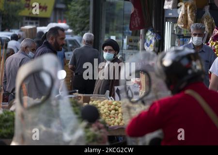 Ein iranischer Geistlicher, der eine schützende Gesichtsmaske trägt, sieht auf, als er neben einem Händler steht, während er am 13. Juni 2021 aus einem Basar (Markt) im Süden Teherans einkauft. Das iranische Volk wird am 18. Juni seine Stimme abgeben, um einen neuen Präsidenten zu wählen. (Foto von Morteza Nikoubazl/NurPhoto) Stockfoto