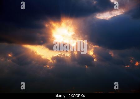 Sonnenstrahlen und rote Strahlen, die durch die dunklen Wolken am wolkigen Himmel leuchten Stockfoto