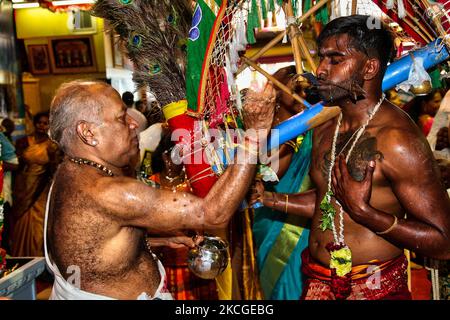 Der tamilische Hindu-Priester spritzt Wasser auf das Gesicht eines Hindu-Anhängers, bevor er ihn segnet, nachdem der Anhänger das Kavadi Attam-Ritual (ein Ritual, bei dem er während des Vinayagar Ther Thiruvizha Festivals in Ontario von Haken in den Rücken getrieben wird) abgeschlossen hat, Kanada am 23. Juli 2006. Die Gläubigen bereiten sich auf die Feier vor, indem sie sich 11 bis 25 Tage vor dem Fest durch Gebet, Zölibat und Fasten reinigen. Während dieses religiösen Festivals zeigen mehrere Anhänger ihre Hingabe, indem sie Opfer darbringen und ihre Körper mit Metallhaken und Spiessen durchstechen. ( Stockfoto