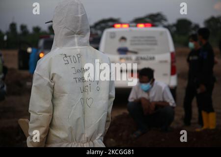 In Schutzkleidung (Hazmat) mit der Aufschrift „Stop, Don't Add More“ (Stop Jangan Nambah Lagi) werden die Leichname des COVID-19 am 26,2021 auf dem öffentlichen Friedhof von Rorotan, North Jakarta, begraben. Die Bestattungsbeamten haben ihre Aufgaben ohne Unterbrechung erfüllt, da es eine Zunahme des Covid-19-Virus-Falles gab, sie begruben die Leichen von etwa 80 bis 100 weiteren Covid-19-Särgen an einem Tag von morgens bis abends. (Foto von Dasril Roszandi/NurPhoto) Stockfoto