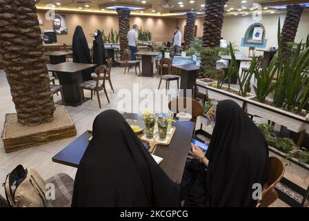 Zwei junge iranische verschleierte Frauen sitzen am 1. Juli 2021 im Nakhlestan Café in der Innenstadt von Teheran zusammen. Das Nakhlestan Cafe (Palm Farm) wurde von der Owj, der Arts and Media Organization des Islamic Revolutionary Guard Corps (IRGS), organisiert und gehört der Organisation, die sich im Stadtzentrum von Teheran befindet. Palm ist das wichtigste Symbol des Iran-Irak-Krieges (1980-88). (Foto von Morteza Nikoubazl/NurPhoto) Stockfoto