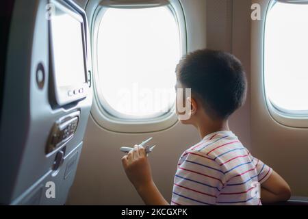 Asiatische Kinder blicken auf den Himmel und die Wolken außerhalb des Flugzeugfensters, während sie auf dem Flugzeugsitz sitzen. Stockfoto