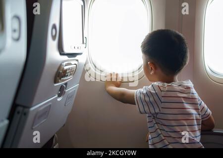 Asiatische Kinder blicken auf den Himmel und die Wolken außerhalb des Flugzeugfensters, während sie auf dem Flugzeugsitz sitzen. Stockfoto