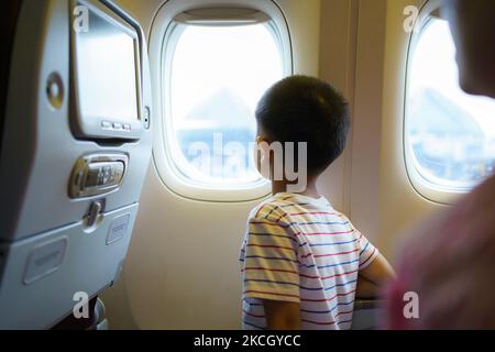 Asiatische Kinder blicken auf den Himmel und die Wolken außerhalb des Flugzeugfensters, während sie auf dem Flugzeugsitz sitzen. Stockfoto