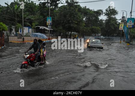 Ein Mann fährt mit ihrer Frau und ihrem kleinen Kind ohne Helm ein Fahrrad, durch eine überflutete Straße nach heftigem Regen in Kalkutta, Indien, am 7. Juli 2021. (Foto von Debarchan Chatterjee/NurPhoto) Stockfoto