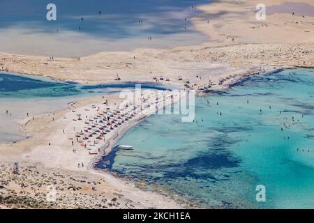 Panoramablick auf den Balos Beach mit den Sonnenschirmen, Sonnendecks und schwimmenden Menschen befindet sich die unglaubliche Lagune mit dem türkisfarbenen exotischen und tropischen Wasser des Mittelmeers in der Region Chania auf der Insel Kreta. Balos ist einer der meistbesuchten Strände Kretas und beliebt bei Besuchern auf der ganzen Welt. Kristallklares Wasser, die Lagune, felsige steile Berge, eine Strandbar mit Sonnenschirmen und Schatten mit Getränken und eine Pirateninsel befinden sich in derselben Region, die mit einem 20-minütigen Trek oder Boot erreichbar ist. Griechenland versucht, seinen Tourismus anzukurbeln und Impfprivilegien zu gewähren Stockfoto