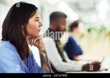 Shes a hard worker. Eine junge Designerin, die in einem Büro mit ihren Kollegen im Hintergrund arbeitet. Stockfoto