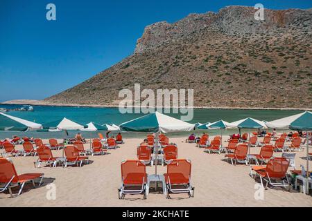 Tourismus in Griechenland - Stavros Beach, in Akrotiri in der Nähe von Chania. Der Strand wurde in den 70s sehr populär, da er Szenen aus dem Film Zorba der Grieche mit Anthony Quinn zeigte. Die Menschen genießen den Schatten des Sonnenschirms und der Sonnenliege einer Strandbar, aber auch andere legen ihr Handtuch hin und entspannen sich während ihres Urlaubs. Der Strand bildet einen kleinen natürlichen Hafen an den Fußstufen des sehr steilen Berges Vardies, wo die Felsen in das kristallklare, türkis-exotische mediterrane Wasser des Strandes eintauchen. Touristen genießen Schwimmen im Wasser der Ägäis, das Sonnenbaden un Stockfoto