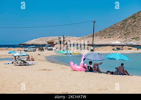 Tourismus in Griechenland - Stavros Beach, in Akrotiri in der Nähe von Chania. Der Strand wurde in den 70s sehr populär, da er Szenen aus dem Film Zorba der Grieche mit Anthony Quinn zeigte. Die Menschen genießen den Schatten des Sonnenschirms und der Sonnenliege einer Strandbar, aber auch andere legen ihr Handtuch hin und entspannen sich während ihres Urlaubs. Der Strand bildet einen kleinen natürlichen Hafen an den Fußstufen des sehr steilen Berges Vardies, wo die Felsen in das kristallklare, türkis-exotische mediterrane Wasser des Strandes eintauchen. Touristen genießen Schwimmen im Wasser der Ägäis, das Sonnenbaden un Stockfoto