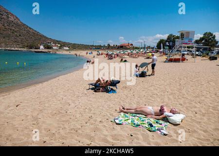 Tourismus in Griechenland - Stavros Beach, in Akrotiri in der Nähe von Chania. Der Strand wurde in den 70s sehr populär, da er Szenen aus dem Film Zorba der Grieche mit Anthony Quinn zeigte. Die Menschen genießen den Schatten des Sonnenschirms und der Sonnenliege einer Strandbar, aber auch andere legen ihr Handtuch hin und entspannen sich während ihres Urlaubs. Der Strand bildet einen kleinen natürlichen Hafen an den Fußstufen des sehr steilen Berges Vardies, wo die Felsen in das kristallklare, türkis-exotische mediterrane Wasser des Strandes eintauchen. Touristen genießen Schwimmen im Wasser der Ägäis, das Sonnenbaden un Stockfoto