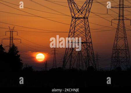 Sommeruntergang in Griechenland mit elektrischen Masten in der Nähe von Thessaloniki. Hochspannungsmasten - Türme während der Sonnenuntergangszeit in der magischen Stunde. Die Metalltürme, wie sie bei Sonnenuntergang auf dem griechischen Land zu sehen sind, verteilen die elektrische Energie aus dem Kraftwerk, in dem Strom in der Kohleproduktion erzeugt wird, im ganzen Land. Die elektrischen Drähte, das Gitter und die Säulen oder Strommasten werden als Silhouetten im farbenprächtigen, wolkigen Abendhimmel in der Dämmerung gesehen. Oreokastro, Thessaloniki in Griechenland am 25. Juli 2021 (Foto von Nicolas Economou/NurPhoto) Stockfoto