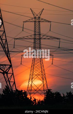 Sommeruntergang in Griechenland mit elektrischen Masten in der Nähe von Thessaloniki. Hochspannungsmasten - Türme während der Sonnenuntergangszeit in der magischen Stunde. Die Metalltürme, wie sie bei Sonnenuntergang auf dem griechischen Land zu sehen sind, verteilen die elektrische Energie aus dem Kraftwerk, in dem Strom in der Kohleproduktion erzeugt wird, im ganzen Land. Die elektrischen Drähte, das Gitter und die Säulen oder Strommasten werden als Silhouetten im farbenprächtigen, wolkigen Abendhimmel in der Dämmerung gesehen. Oreokastro, Thessaloniki in Griechenland am 25. Juli 2021 (Foto von Nicolas Economou/NurPhoto) Stockfoto