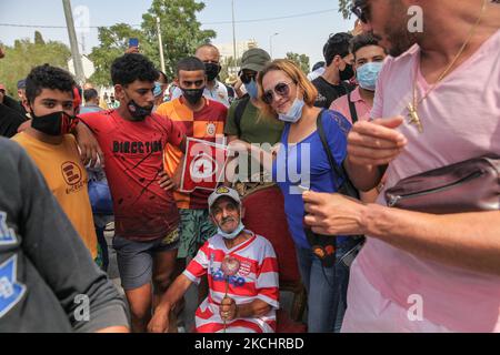 Ein Anhänger von Kais Saied hält eine Zwiebel in der Hand und posiert mit Demonstranten, während er während einer Demonstration vor dem Gebäude des tunesischen parlaments in Bardo, in der Hauptstadt Tunis, Tunesien, am 26. Juli 2021 auf einem Stuhl sitzt. Um den tunesischen Präsidenten Kai Saied nach seiner Entscheidung, die Regierung von Hichem Mechichi zu entlassen, zu unterstützen, das parlament einzufrieren und die Immunität aller Mitglieder des parlaments auszusetzen. (Foto von Chedly Ben Ibrahim/NurPhoto) Stockfoto