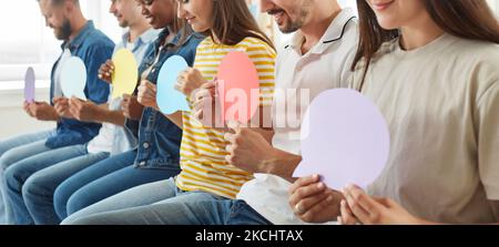 Eine Gruppe von jungen, unterschiedlichen Menschen, die in Reihe sitzen und Sprechballons in Mock-up halten Stockfoto