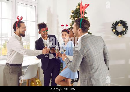 Menschen, die neben dem Weihnachtsbaum stehen und an Silvester mit einem Glas Champagner anstoßen Stockfoto