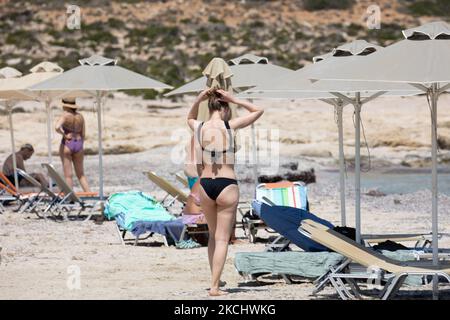 Menschen, Männer und Frauen mit Bikini und Badeanzug genießen das Wasser des Balos Beach oder den Schatten unter einem Schirm der lokalen Strandbar an der unglaublichen Lagune, mit dem Pool wie türkisblaues exotisches und tropisches Wasser des Mittelmeers befindet sich in der Region Chania auf der Insel Kreta. Balos ist einer der meistbesuchten Strände Kretas und beliebt bei Besuchern auf der ganzen Welt. Kristallklares Wasser, die Lagune, felsige steile Berge, eine Strandbar mit Sonnenschirmen und Schatten mit Getränken und eine Pirateninsel befinden sich in derselben Region, die mit einem 20-minütigen Trek oder Boot erreichbar ist. Griechenland ist TRY Stockfoto