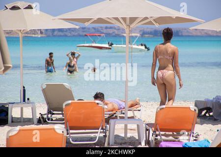 Menschen, Männer und Frauen mit Bikini und Badeanzug genießen das Wasser des Balos Beach oder den Schatten unter einem Schirm der lokalen Strandbar an der unglaublichen Lagune, mit dem Pool wie türkisblaues exotisches und tropisches Wasser des Mittelmeers befindet sich in der Region Chania auf der Insel Kreta. Balos ist einer der meistbesuchten Strände Kretas und beliebt bei Besuchern auf der ganzen Welt. Kristallklares Wasser, die Lagune, felsige steile Berge, eine Strandbar mit Sonnenschirmen und Schatten mit Getränken und eine Pirateninsel befinden sich in derselben Region, die mit einem 20-minütigen Trek oder Boot erreichbar ist. Griechenland ist TRY Stockfoto