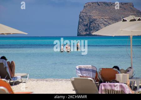 Menschen, Männer und Frauen mit Bikini und Badeanzug genießen das Wasser des Balos Beach oder den Schatten unter einem Schirm der lokalen Strandbar an der unglaublichen Lagune, mit dem Pool wie türkisblaues exotisches und tropisches Wasser des Mittelmeers befindet sich in der Region Chania auf der Insel Kreta. Balos ist einer der meistbesuchten Strände Kretas und beliebt bei Besuchern auf der ganzen Welt. Kristallklares Wasser, die Lagune, felsige steile Berge, eine Strandbar mit Sonnenschirmen und Schatten mit Getränken und eine Pirateninsel befinden sich in derselben Region, die mit einem 20-minütigen Trek oder Boot erreichbar ist. Griechenland ist TRY Stockfoto