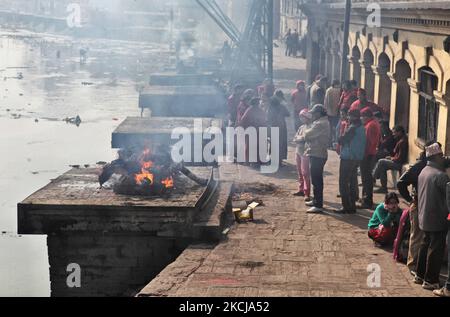 Zuschauer beobachten, wie am 10. Dezember 2011 am Ufer des Bagmati-Flusses im Pashupatinath-Tempel in Kathmandu, Nepal, ein Scheiterhaufen in Flammen umgehüllt wird. Nach hinduistischer Religion und Tradition müssen die Toten eingeäschert werden. Die Körper werden nach dem Brauch eingeäschert und die Asche und die Überreste werden in die heiligen Wasser gefegt. Die Bagmati verläuft weiter südlich in den Ganges und gilt für Hindus gleichermaßen heilig. Der Komplex in Pashupatinath ist der heiligste Hindu-Ort in Nepal. (Foto von Creative Touch Imaging Ltd./NurPhoto) Stockfoto