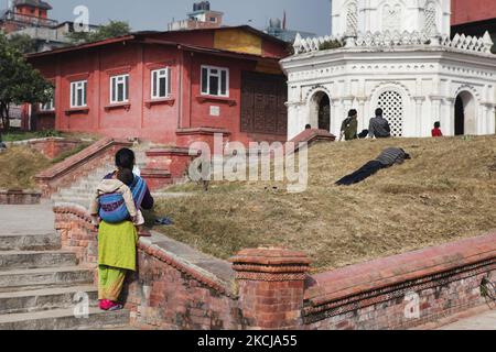 Die Frau mit ihrem Kind in einer Schlinge auf dem Rücken ruht am 10. Dezember 2011 im Pashupatinath-Tempelkomplex in Kathmandu, Nepal. Andere Anhänger entspannen sich auf einem kleinen Grasfeld zwischen alten Tempeln, nachdem sie Gebete dargebracht haben. Der Komplex in Pashupatinath ist der heiligste Hindu-Ort in Nepal. (Foto von Creative Touch Imaging Ltd./NurPhoto) Stockfoto