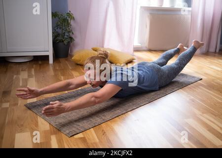 Reife Frau, die drinnen trainiert und eine Navasana-Variation-Pose macht. Stockfoto