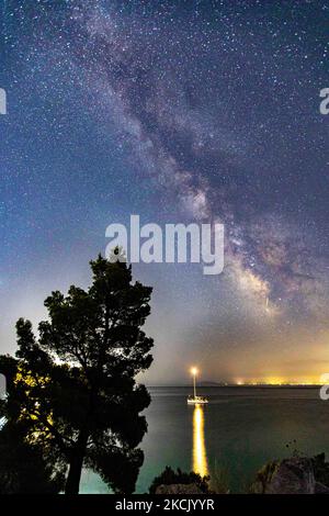 Die Milchstraße im dunklen griechischen Nachthimmel mit den leuchtenden Sternen, Teil der Galaxie, die unser Sonnensystem enthält, wie von einem Sandstrand in Chalkidiki, Griechenland aus gesehen, mit einem sichtbaren Boot und Dörfern auf der anderen Seite, die das Licht auf der Wasseroberfläche reflektieren. Die Langzeitaufnahmen der Milchstraße wurden vom Koviou-Sandstrand, einer typischen mediterranen Landschaft der Ägäis, in der Nähe von Nikiti aufgenommen. Aufgrund der Coronavirus-Pandemie Covid-19 war Griechenland nicht überfüllt mit Touristen und Sicherheitsmassnahmen, die während der Sommerzeit angewendet wurden, was dazu beigetragen hat, dass der Himmel dunkler und dunkler wurde Stockfoto