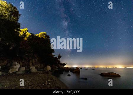 Die Milchstraße im dunklen griechischen Nachthimmel mit den leuchtenden Sternen, Teil der Galaxie, die unser Sonnensystem enthält, wie von einem Sandstrand in Chalkidiki, Griechenland aus gesehen, mit einem sichtbaren Boot und Dörfern auf der anderen Seite, die das Licht auf der Wasseroberfläche reflektieren. Die Langzeitaufnahmen der Milchstraße wurden vom Koviou-Sandstrand, einer typischen mediterranen Landschaft der Ägäis, in der Nähe von Nikiti aufgenommen. Aufgrund der Coronavirus-Pandemie Covid-19 war Griechenland nicht überfüllt mit Touristen und Sicherheitsmassnahmen, die während der Sommerzeit angewendet wurden, was dazu beigetragen hat, dass der Himmel dunkler und dunkler wurde Stockfoto