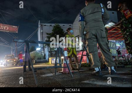 Beamte stehen am 23. August 2021 am Eingang eines Wohnkomplexes, wo im Dorf South Birobuli, Stadt Palu, Provinz Zentral-Sulawesi, Indonesien, eine effektive Mikroschleuse angebracht wird, Wache. Die lokale Regierung hat Lock Micro Effective (LME) in mehreren städtischen Dörfern der Stadt eingeführt, um die Übertragung von COVID -19 zu reduzieren, die im August auf mehr als 200 Prozent ansteigt. Diese Aussperrung schließt das ein- und Aussteigen des Komplexes ein und muss die Ergebnisse eines schnellen Antigen-Tests zeigen. Der Bedarf an Nahrungsmitteln und Getränken für die von der Politik betroffenen Bewohner ist nicht gut Stockfoto