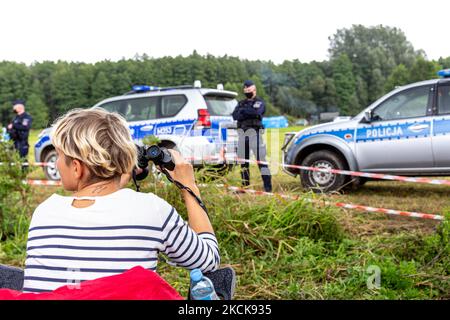 Aktivisten protestieren, während Soldaten der polnischen Armee eine Gruppe von Einwanderern aus Afghanistan an der weißrussischen Grenze umkreisen und ihre Einreise in das Land in Usnarz Gorny, Polen, am 27. August 2021 verhindern. Die Armee und die Polizei hielten die Migranten an der Grenze an und verhinderten, dass sie nach Polen einmarschieren konnten, die Armee verweigerte auch den Zugang zu Asylverfahren, medizinischer Hilfe und Lebensmitteln. Journalisten und Wohltätigkeitsarbeiter werden etwa 300 Meter entfernt gehalten. Die Aktionen der polnischen Regierung wurden weithin kritisiert. Die polnische Regierung beschloss auch, einen Zaun zu bauen, um dem Zustrom von Wanderern ein Ende zu setzen Stockfoto