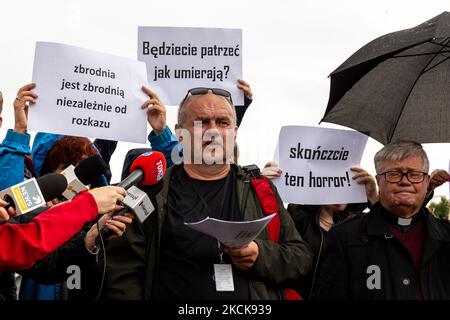 Aktivisten protestieren, während Soldaten der polnischen Armee eine Gruppe von Einwanderern aus Afghanistan an der weißrussischen Grenze umkreisen und ihre Einreise in das Land in Usnarz Gorny, Polen, am 27. August 2021 verhindern. Die Armee und die Polizei hielten die Migranten an der Grenze an und verhinderten, dass sie nach Polen einmarschieren konnten, die Armee verweigerte auch den Zugang zu Asylverfahren, medizinischer Hilfe und Lebensmitteln. Journalisten und Wohltätigkeitsarbeiter werden etwa 300 Meter entfernt gehalten. Die Aktionen der polnischen Regierung wurden weithin kritisiert. Die polnische Regierung beschloss auch, einen Zaun zu bauen, um dem Zustrom von Wanderern ein Ende zu setzen Stockfoto