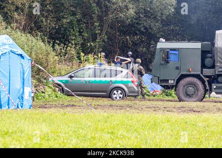 Soldaten der polnischen Armee umkreisen eine Gruppe von Einwanderern aus Afghanistan an der weißrussischen Grenze und verhindern ihre Einreise in das Land in Usnarz Gorny, Polen, am 27. August 2021. Die Armee und die Polizei hielten die Migranten an der Grenze an und verhinderten, dass sie nach Polen einmarschieren konnten, die Armee verweigerte auch den Zugang zu Asylverfahren, medizinischer Hilfe und Lebensmitteln. Journalisten und Wohltätigkeitsarbeiter werden etwa 300 Meter entfernt gehalten. Die Aktionen der polnischen Regierung wurden weithin kritisiert. Die polnische Regierung beschloss außerdem, einen Zaun zu errichten, um dem Zustrom von Migranten, die über Belarus wandern, ein Ende zu setzen b Stockfoto