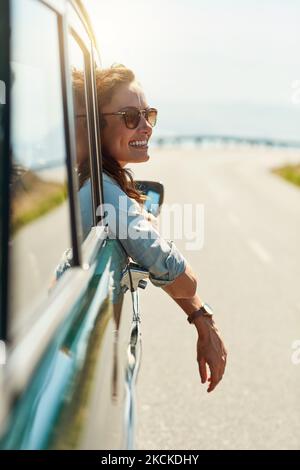 Die Freiheit der offenen Straße. Eine attraktive Frau, die beim Autoreise aus einem Autofenster hängt. Stockfoto