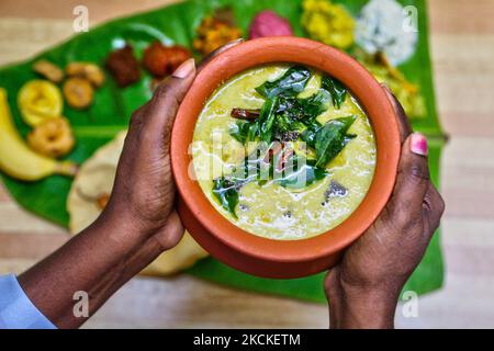 Frau hält einen Topf mit Maambazha pulissery (Mangoquark-Currys), während sie während des Onam Festivals am 28. August 2021 in Toronto, Ontario, Kanada, eine traditionelle Sadhya-Mahlzeit auf einem Bananenblatt serviert. Sadhya besteht aus einer Vielzahl von traditionellen vegetarischen Gerichten, die auf einem Bananenblatt serviert werden und ist bei Feiern und Festen im indischen Bundesstaat Kerala üblich. Sadhya bedeutet Bankett in Malayalam. Onam ist ein Erntefest und eines von drei großen jährlichen hinduistischen Feiern zusammen mit Vishu und Thiruvathira, die von Keraliten beobachtet werden. (Foto von Creative Touch Imaging Ltd./NurPhoto) Stockfoto