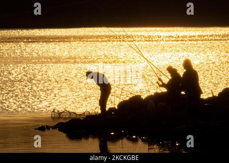 Die Menschen fischen am See am frühen Morgen, während die Sonne auf dem Wasser reflektiert wird. Magische Stunde Sommer Sonnenaufgang mit warmen Farben des Himmels und der Sonne über Kerkini mit Vögeln, Pferden, lokalen Fischern als Silhouetten gefischt, am See Nationalpark in Serres Region in Nordgriechenland. Der künstliche Kerkini-See ist ein einzigartiges Feuchtgebiet, ein Nationalpark und durch die Ramsar-Konvention als Feuchtgebiet mit Tausenden von Vögeln geschützt, darunter seltene und geschützte Flusswälder, da sich wichtige Hydrobiosphären entwickeln, die von großer internationaler Bedeutung und Akzeptanz sind, die wichtigste Wasserquelle Stockfoto