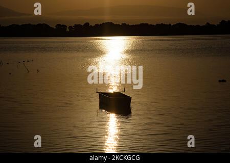 Fischerboot in Kerkini See. Magische Stunde Sommer Sonnenaufgang mit warmen Farben des Himmels und der Sonne über Kerkini mit Vögeln, Pferden, lokalen Fischern als Silhouetten gefischt, am See Nationalpark in Serres Region in Nordgriechenland. Der künstliche Kerkini-See ist ein einzigartiges Feuchtgebiet, ein Nationalpark und durch die Ramsar-Konvention als Feuchtgebiet mit Tausenden von Vögeln geschützt, darunter seltene und geschützte Flusswälder, da sich wichtige Hydrobiosphären entwickeln, die von großer internationaler Bedeutung und Akzeptanz sind, Die Hauptwasserquelle des Flusses Strymon stammt aus Bulgarien. Kerkini Lake Stockfoto