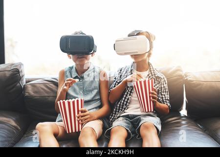 Sie leben den Film. Ein Bruder und eine Schwester essen Popcorn und sehen sich Filme mit Virtual-Reality-Headsets zu Hause an. Stockfoto